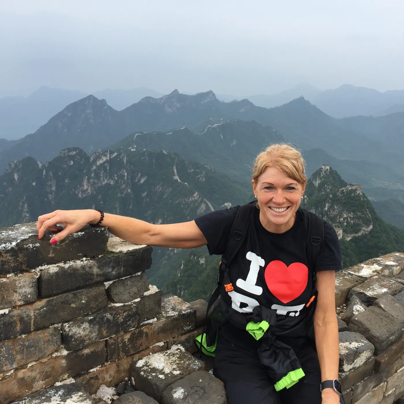 Caro Syson, founder of Your Final Matters, smiling on the Great Wall of China with mountains behind her