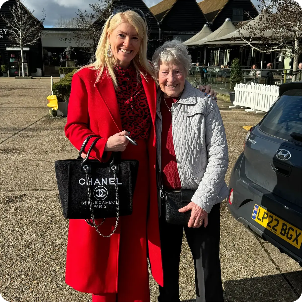 Caro Syson, founder of Your Final Matters, in a red coat, standing with an older woman outdoors