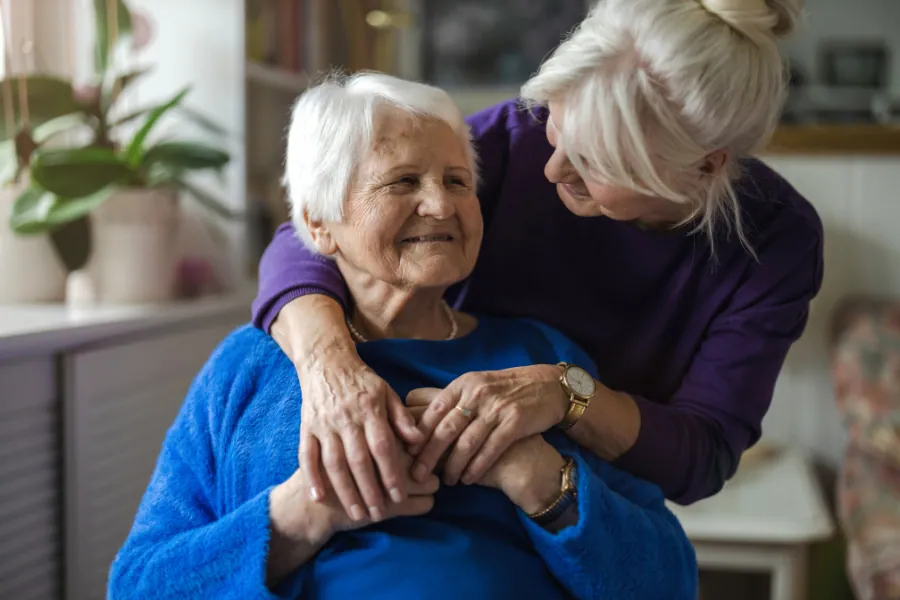 Younger woman hugging an older woman from behind, both smiling