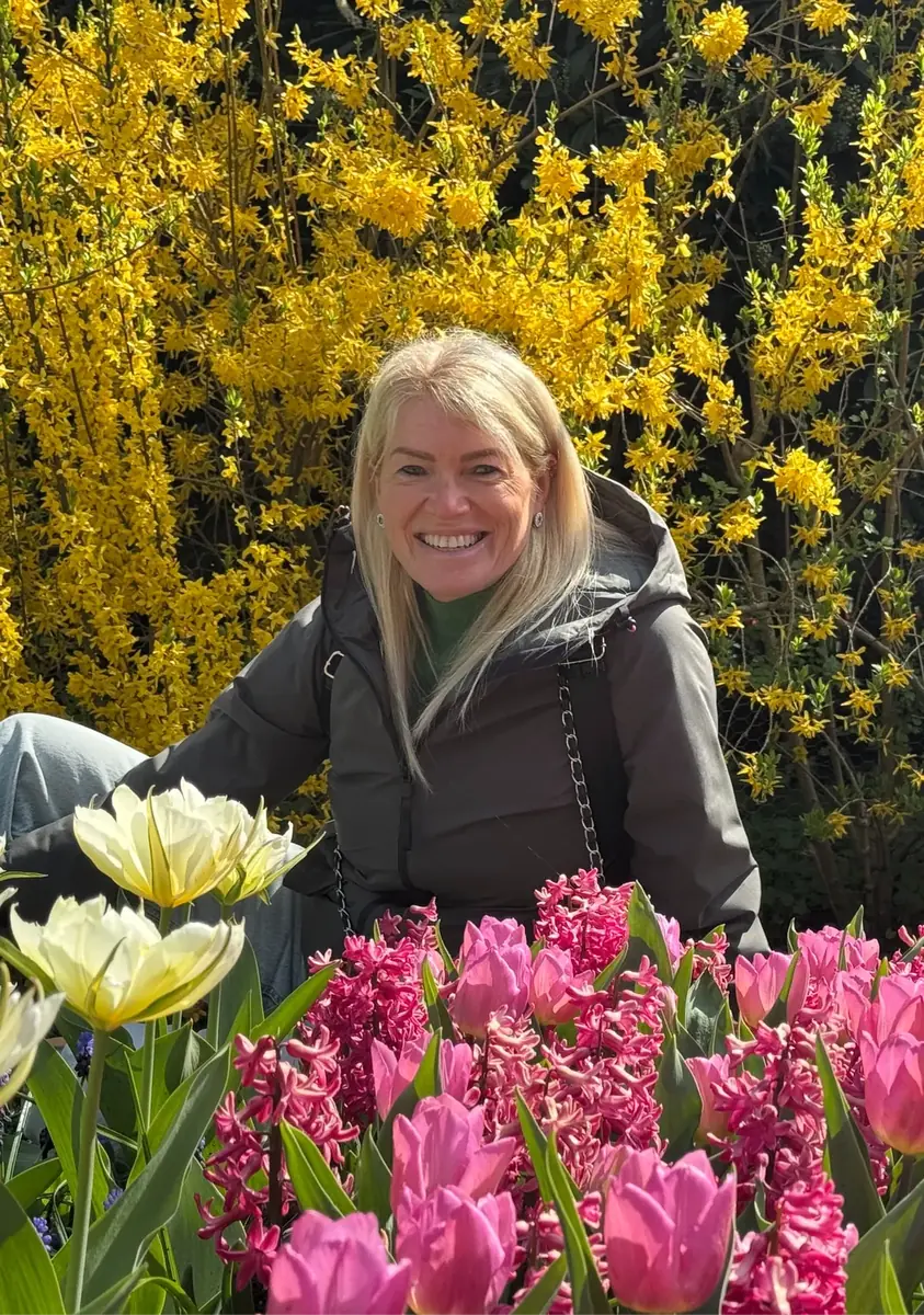 Caro Syson, founder of Your Final Matters, smiling among spring flowers and tulips